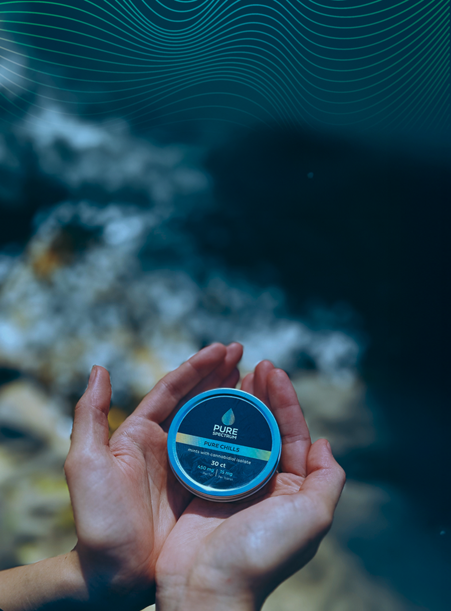 Hands holding a Pure Spectrum CBD tin beside a mountain stream