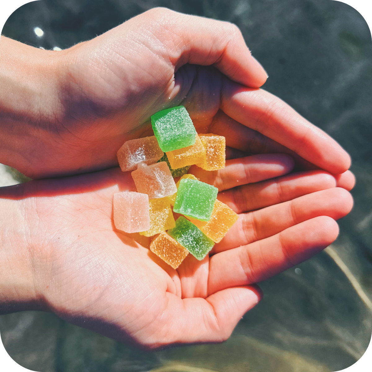 Assorted vegan Pure Spectrum CBD gummies in cupped hands, vibrant natural lighting